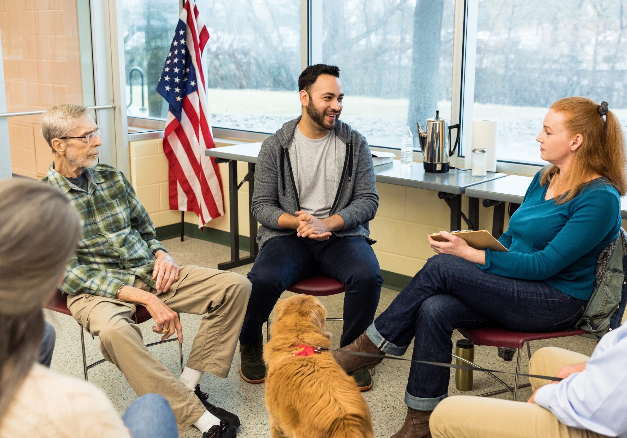 A diverse group of veterans, including an emotional support dog, meet at the community center for a therapy session.